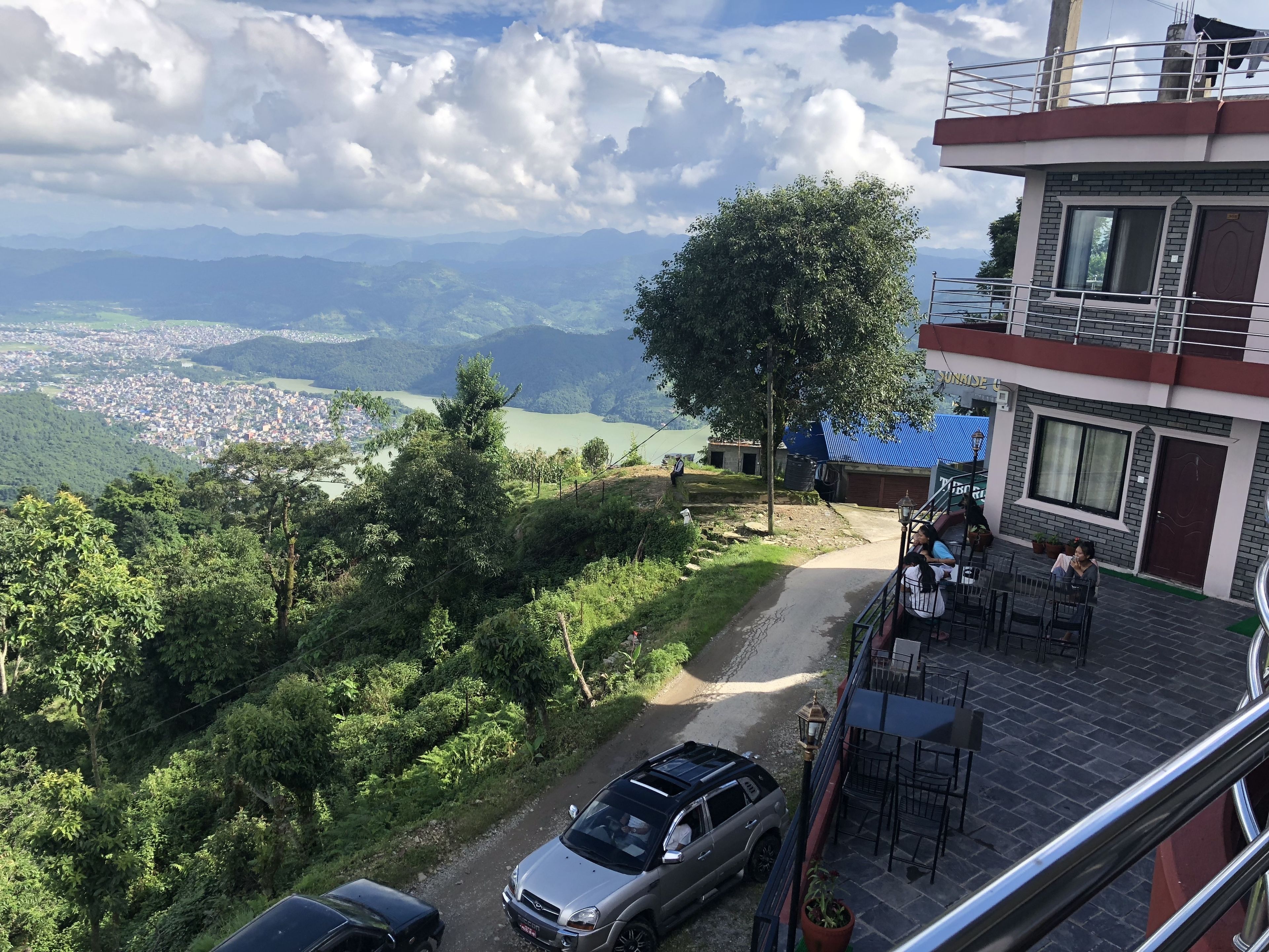 Un hôtel doté d’une terrasse, offrant une vue sur une vallée, et devant lequel se trouve une voiture garée.