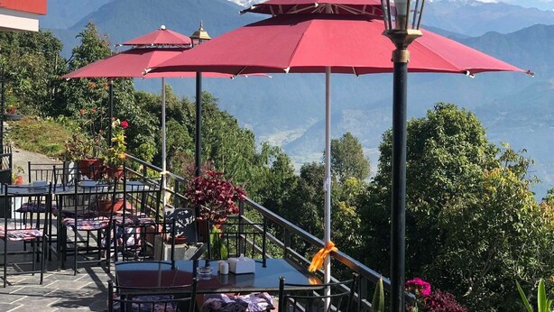 Ein Sitzbereich im Freien mit roten Sonnenschirmen, Tischen und Stühlen mit Blick auf eine gebirgige Landschaft.
