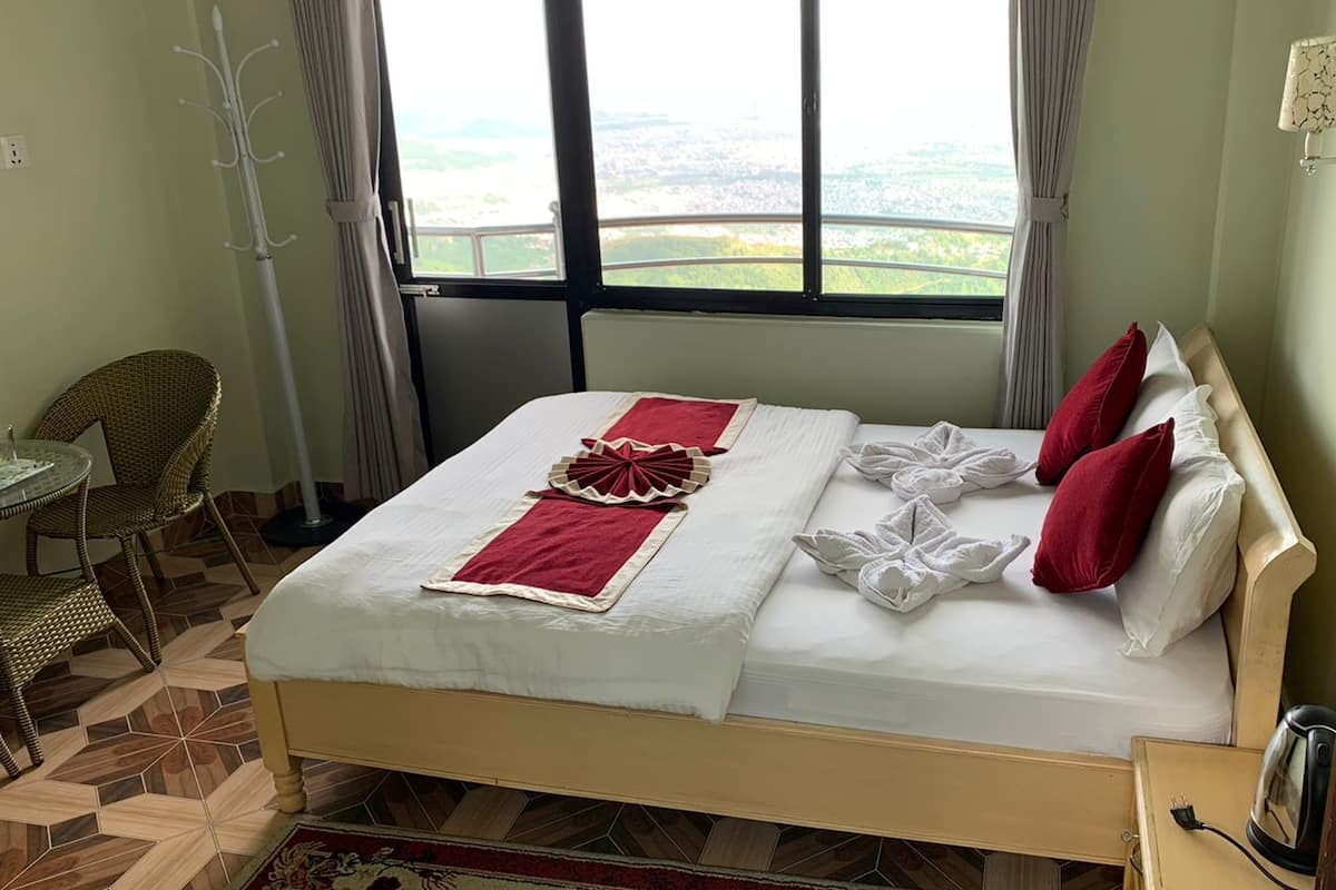 Una habitación de hotel con cama, una mesa y sillas, y vistas a la ciudad a través de amplios ventanales.
