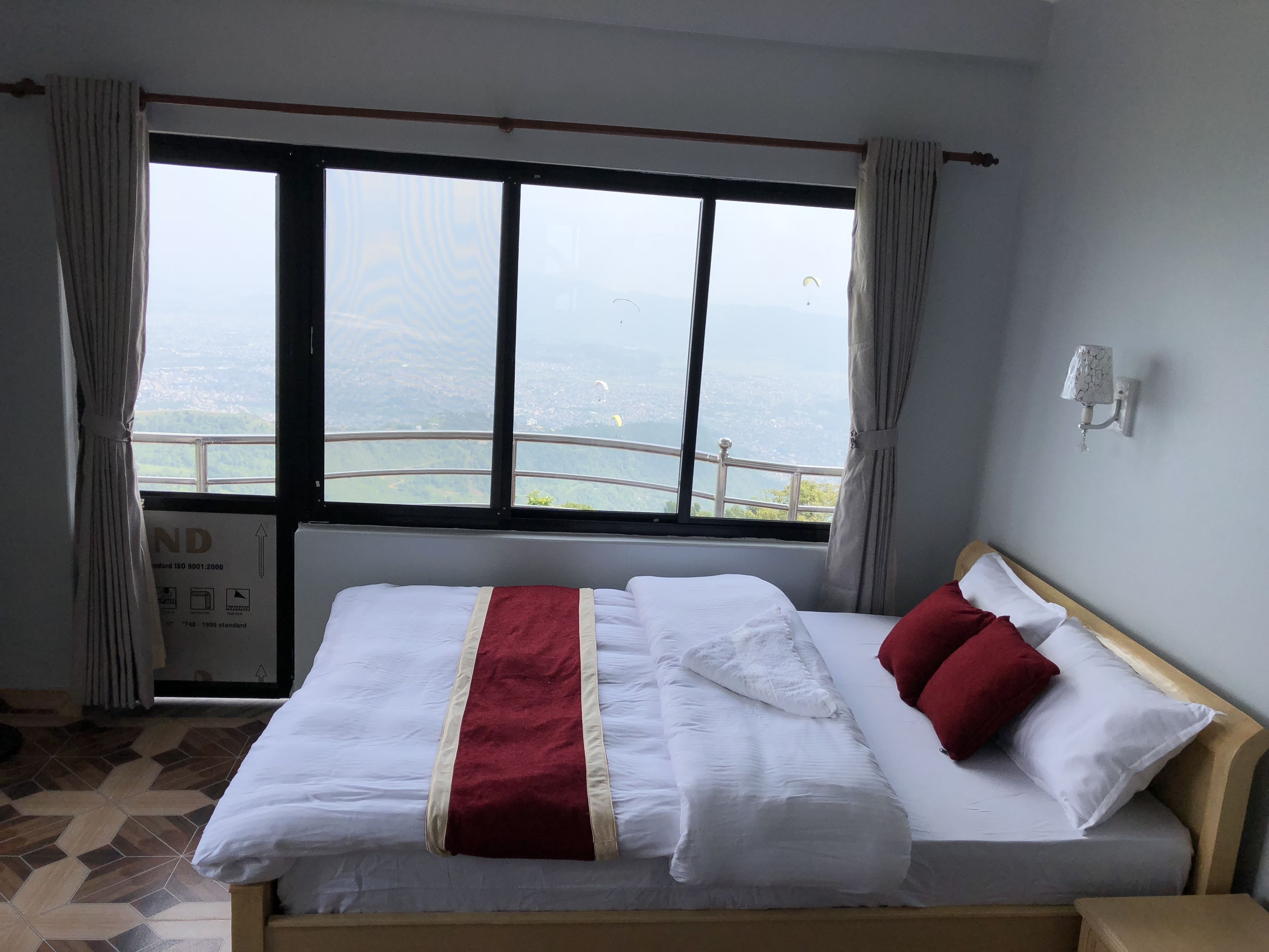 Een hotelkamer met een groot bed, uitzicht op de stad door het raam en een bordje dat de standaard van de kamer aangeeft.