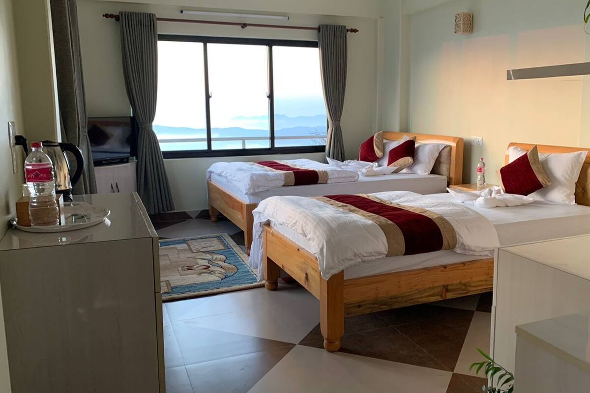 Habitación de hotel con dos camas, un escritorio, una ventana con vistas y una pequeña alfombra.
