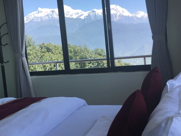 Een hotelkamer met een bed, gordijnen en een raam met uitzicht op de bergen.