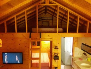 Ein gemütliches Blockhaus mit Schlafzimmer auf dem Dachboden, einer kleinen Küche und einem Fernseher.