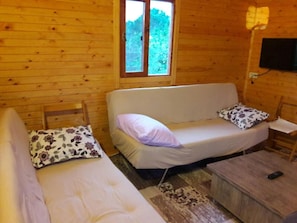 Ein Holzblock-Innenraum mit Schlafsofa, zwei Kissen, einem kleinen Tisch und einem Fenster.