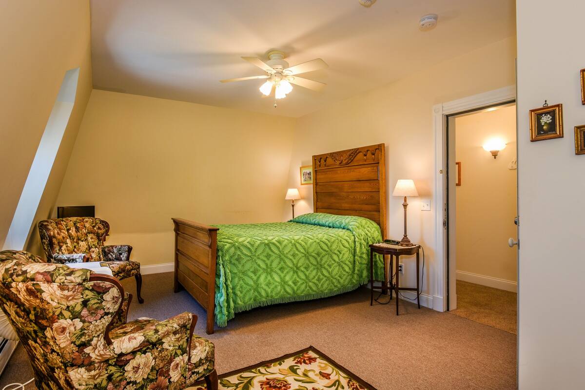 A bedroom with a bed, a chair, a dresser, a lamp, and a ceiling fan.