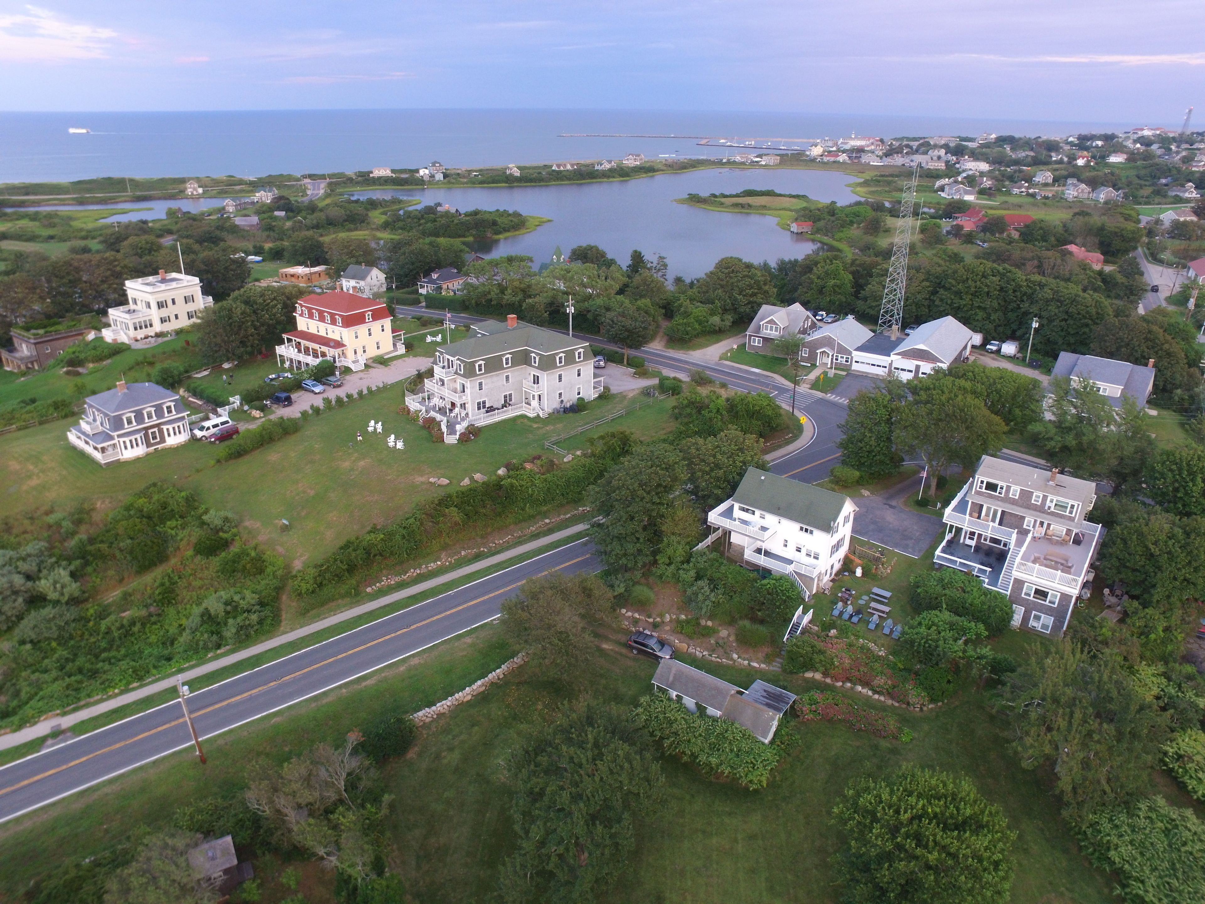 An aerial view of a coastal town with a prominent waterfront, a large white building with a red roof, and a road running through the center.
