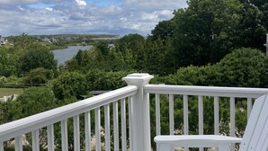 A deck with white railings and chairs overlooking a river and greenery. - Payne's Harbor View Inn (Block Island)