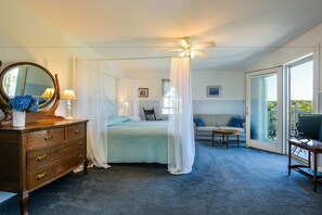 A bedroom with a four-drawer dresser, a canopy bed, a ceiling fan, a sofa, a television, and a large window.