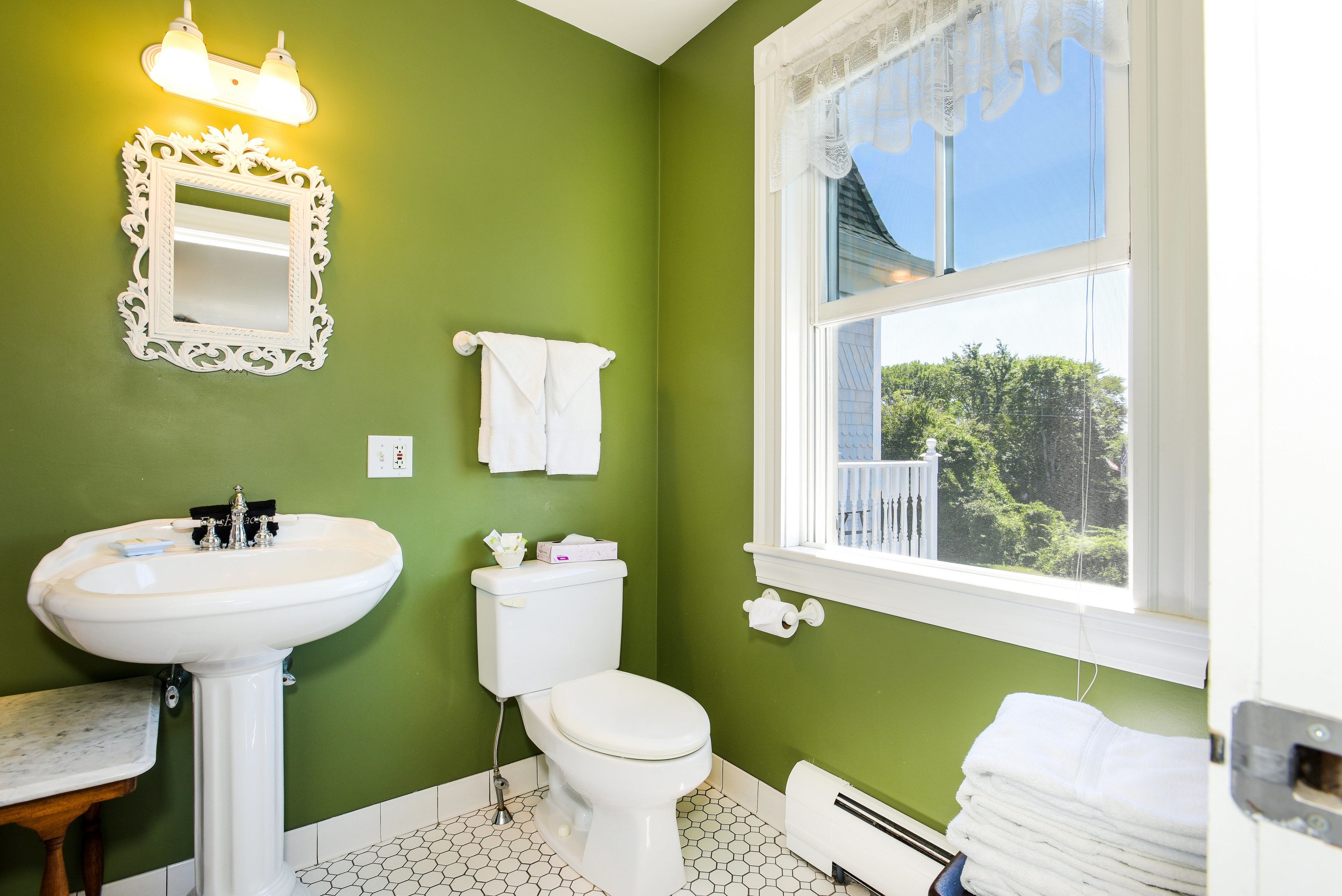 A bathroom with a green wall, white sink, toilet, and a window with a view of greenery.