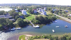 An aerial view of a lakeside community with multiple houses, a dock with boats, and a road running parallel to the water. - Payne's Harbor View Inn (Block Island)