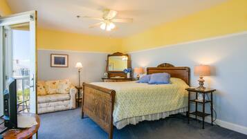 A bedroom with a bed, a wooden headboard, a bedside table with a lamp, a nightstand, a chair, a window, and a ceiling fan.