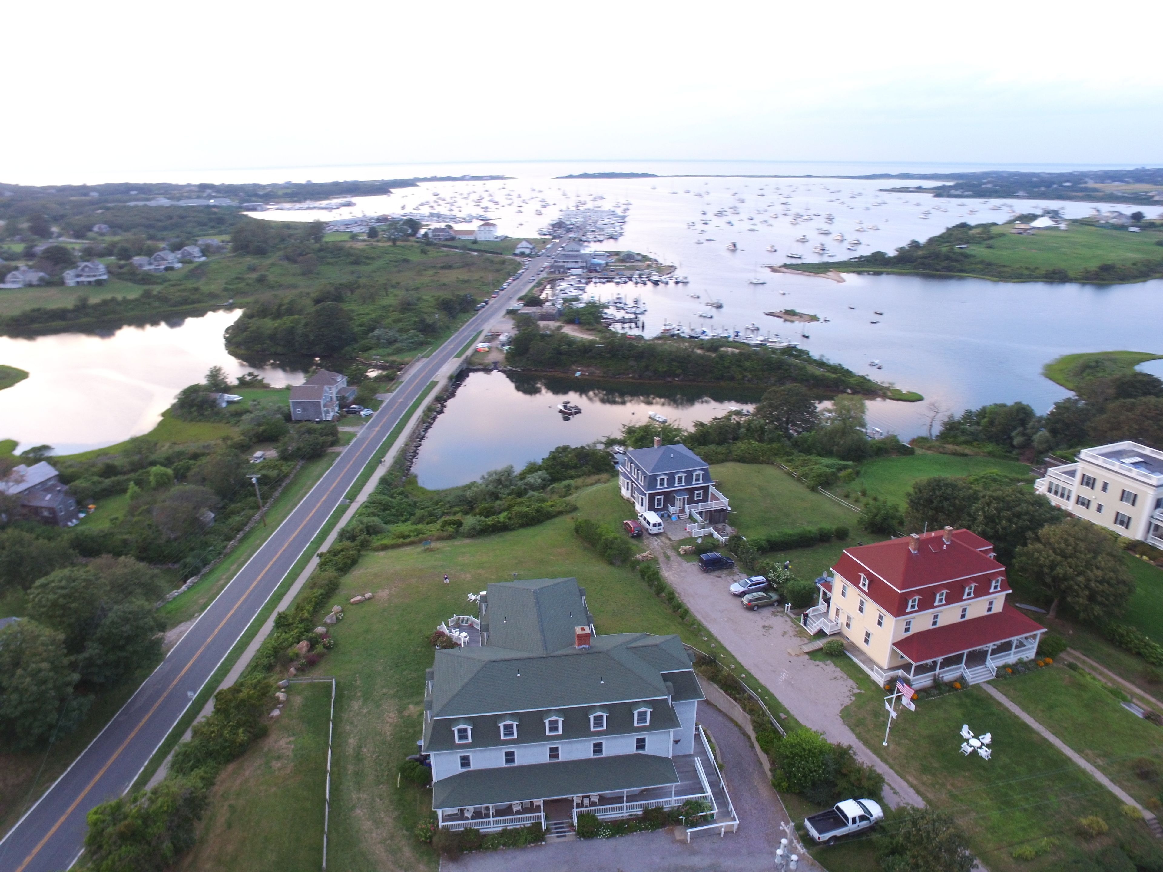 An aerial view of a coastal area with a road, several houses, and a marina with boats.