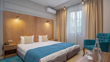 A hotel room with a large bed, a wooden headboard, a blue accent wall, a teal armchair, a wooden side table, and a bottle of water on the table.