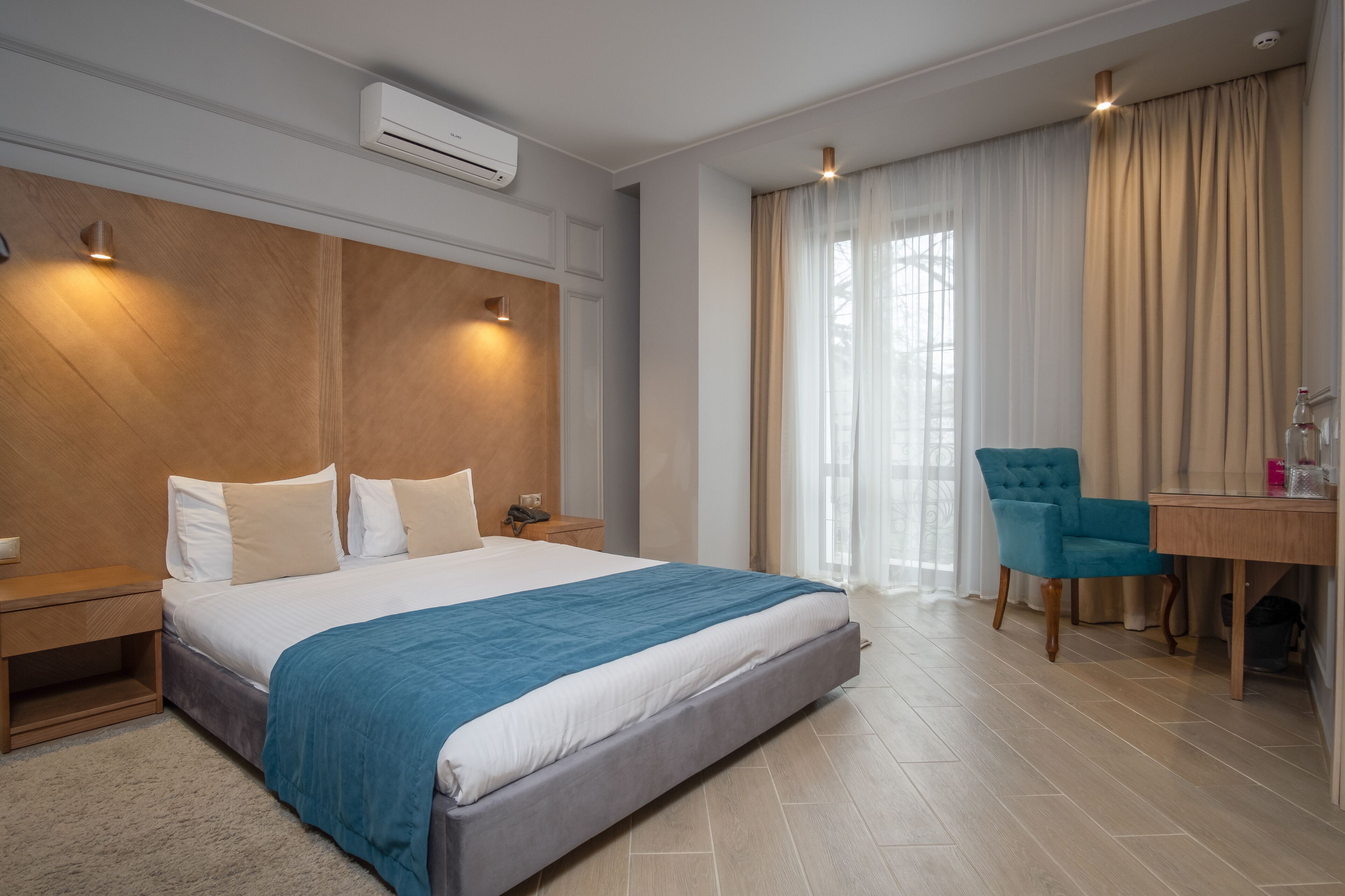 A modern hotel room with a large bed, a desk with a chair, and a window with curtains.