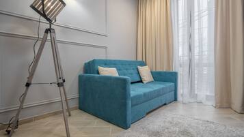 A modern living room with a teal sofa, a standing floor lamp, and a large window with sheer curtains.