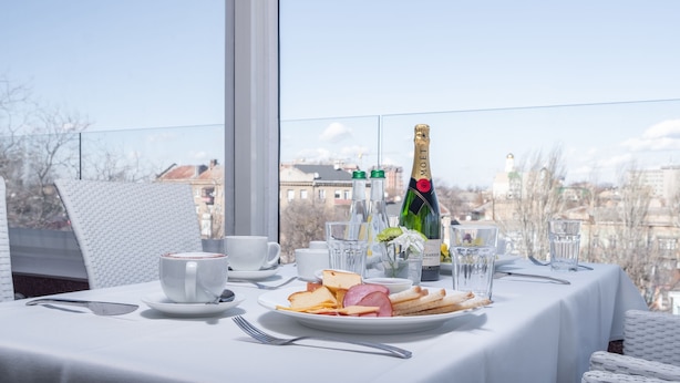 A table set with a plate of food, glasses, a bottle of champagne, and a white tablecloth.