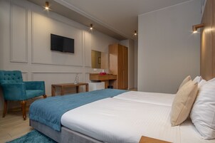 Una habitación de hotel moderna con una cama grande, un televisor montado en la pared, un armario de madera, un escritorio pequeño y un sillón azul aguamarina.