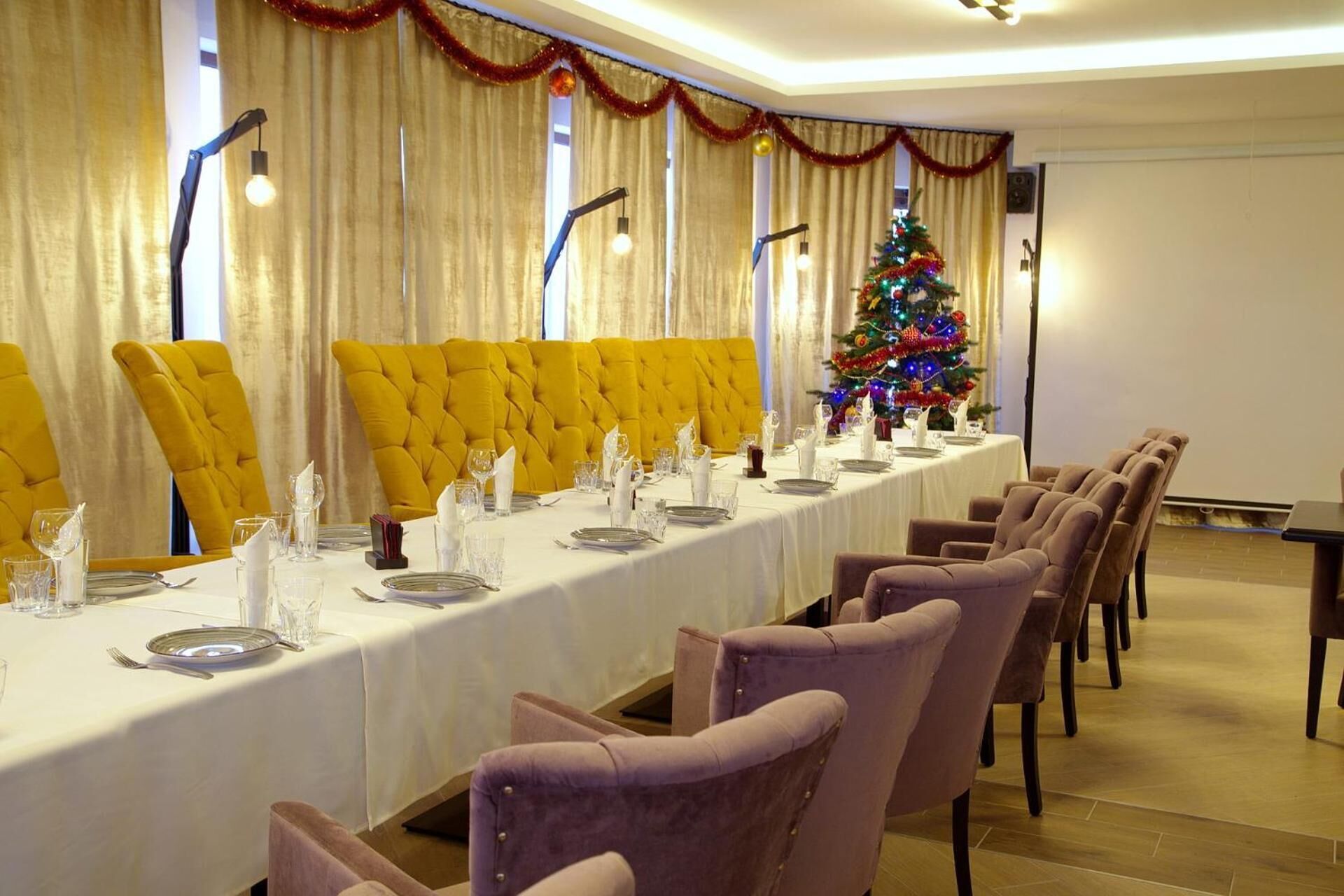 A long dining table set for a meal, with yellow and purple chairs, a Christmas tree, and a chandelier.
