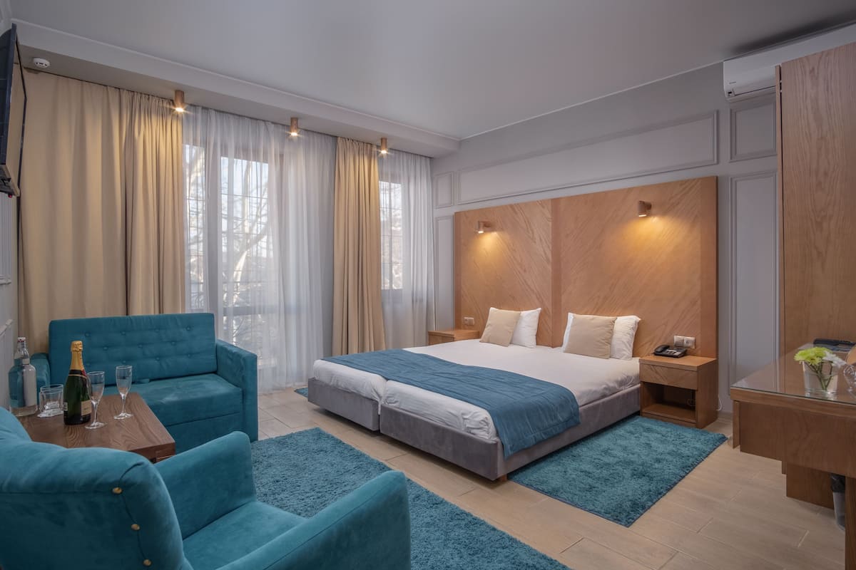 Een moderne slaapkamer met een groot bed, een blauwe bank, een houten nachtkastje en een bureau met een vaas.