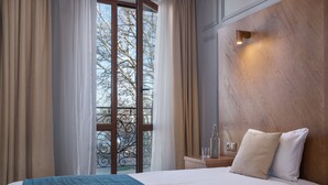 A hotel room with a large bed, a wooden headboard, a nightstand with a glass, and a view of a balcony with metal railings.