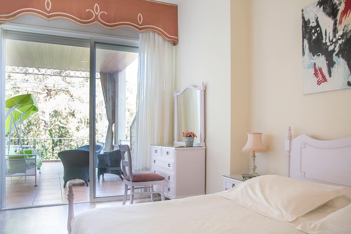A bedroom with a bed, a dresser, a chair, a mirror, and a balcony with a chair and umbrella.