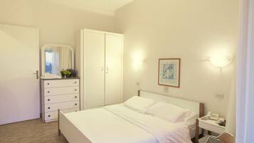 A hotel room with a bed, a dresser, a mirror, a bedside table with a phone, and a wall-mounted light fixture.