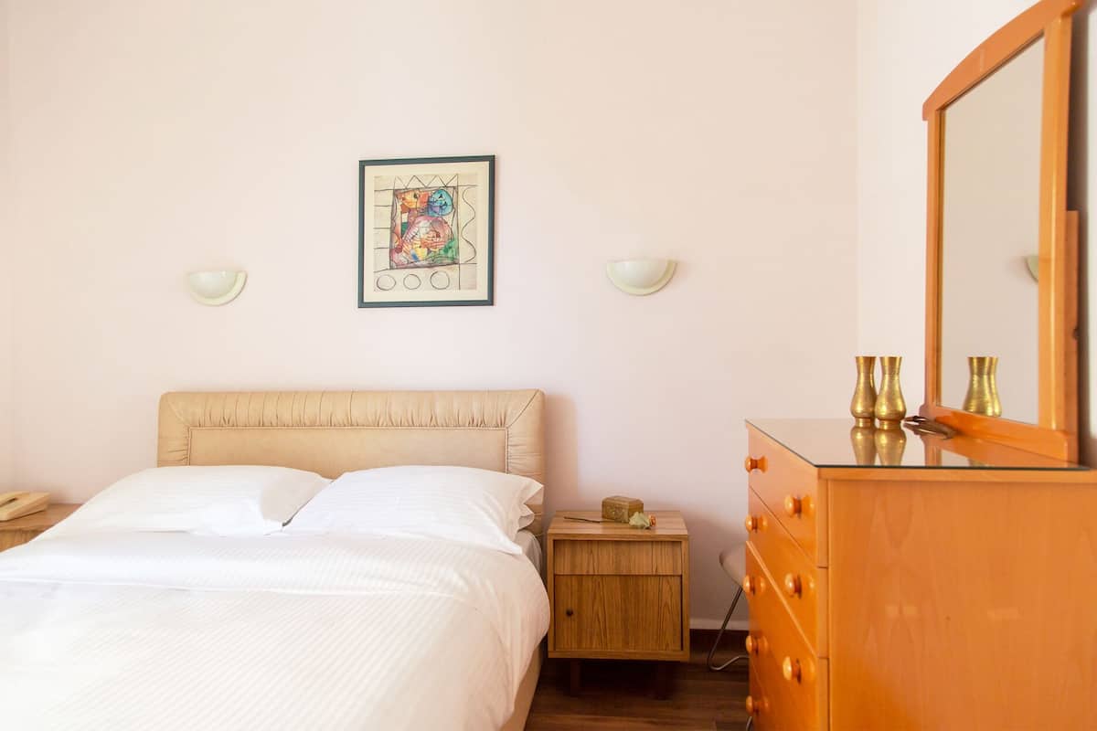 A bedroom with a bed, bedside table, nightstand, dresser, mirror, and a framed picture on the wall.