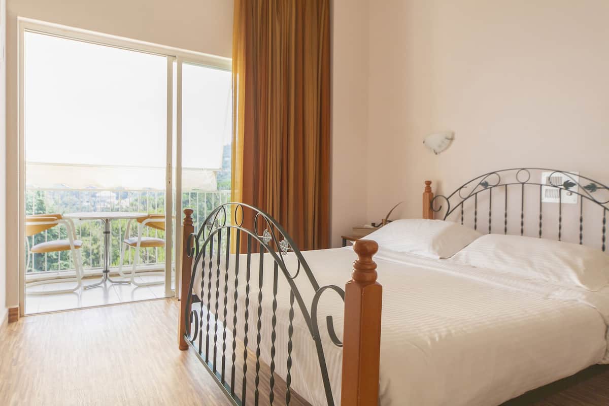 A bedroom with a bed, a window with curtains, and a balcony with chairs.