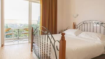 Un dormitorio con cama, ventana con cortinas y balcón con sillas.