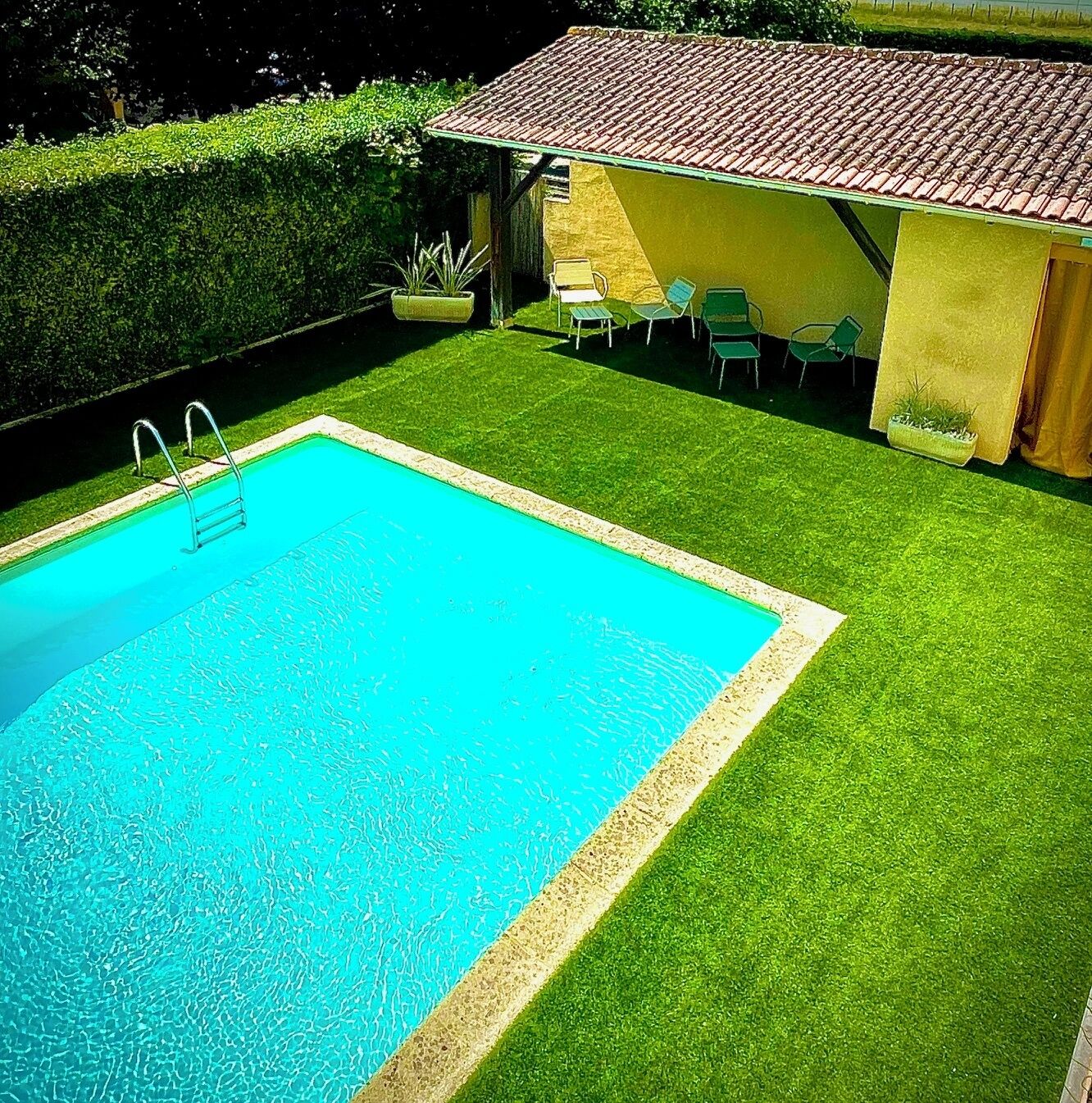 Une piscine rectangulaire avec un escalier, entourée d’une pelouse bien entretenue et d’un petit bâtiment doté d’un toit en tuiles.