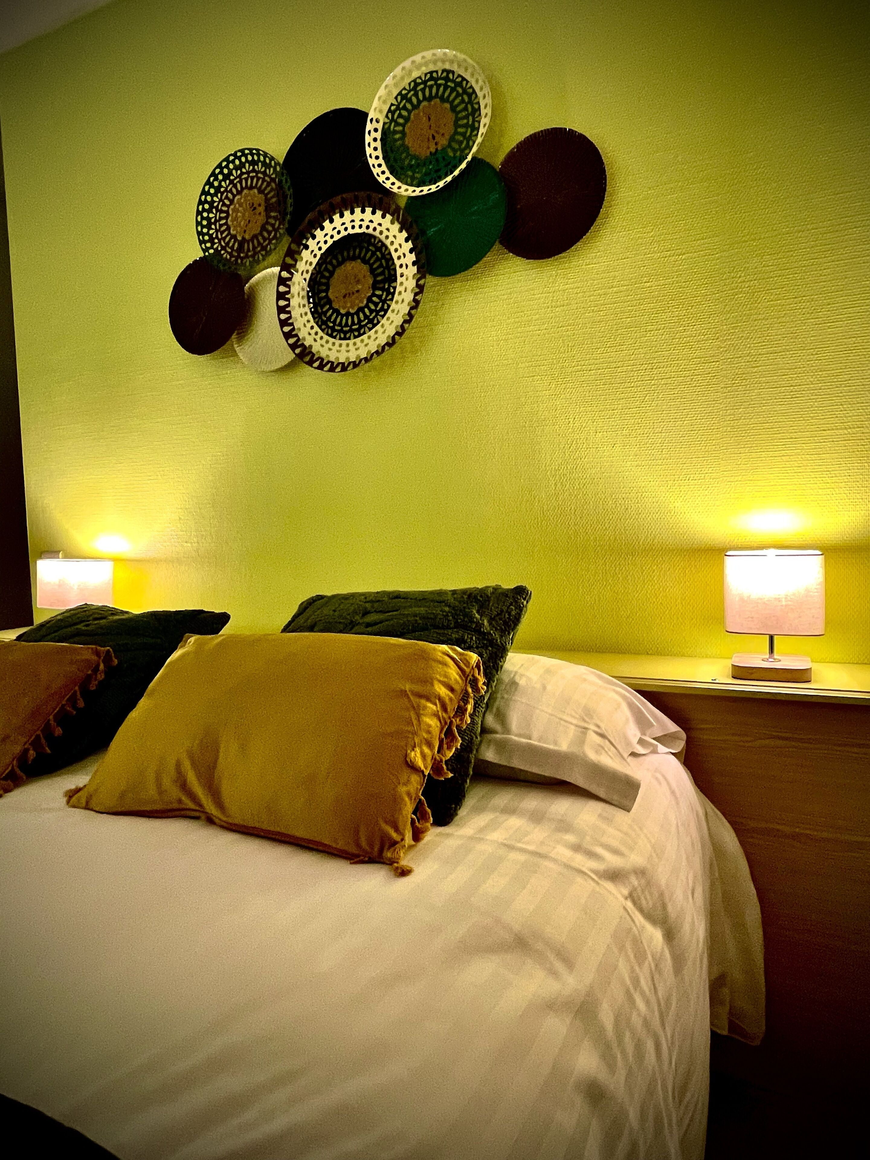 Un lit recouvert de draps blancs, plusieurs oreillers de différentes couleurs et un mur orné de motifs circulaires décoratifs.