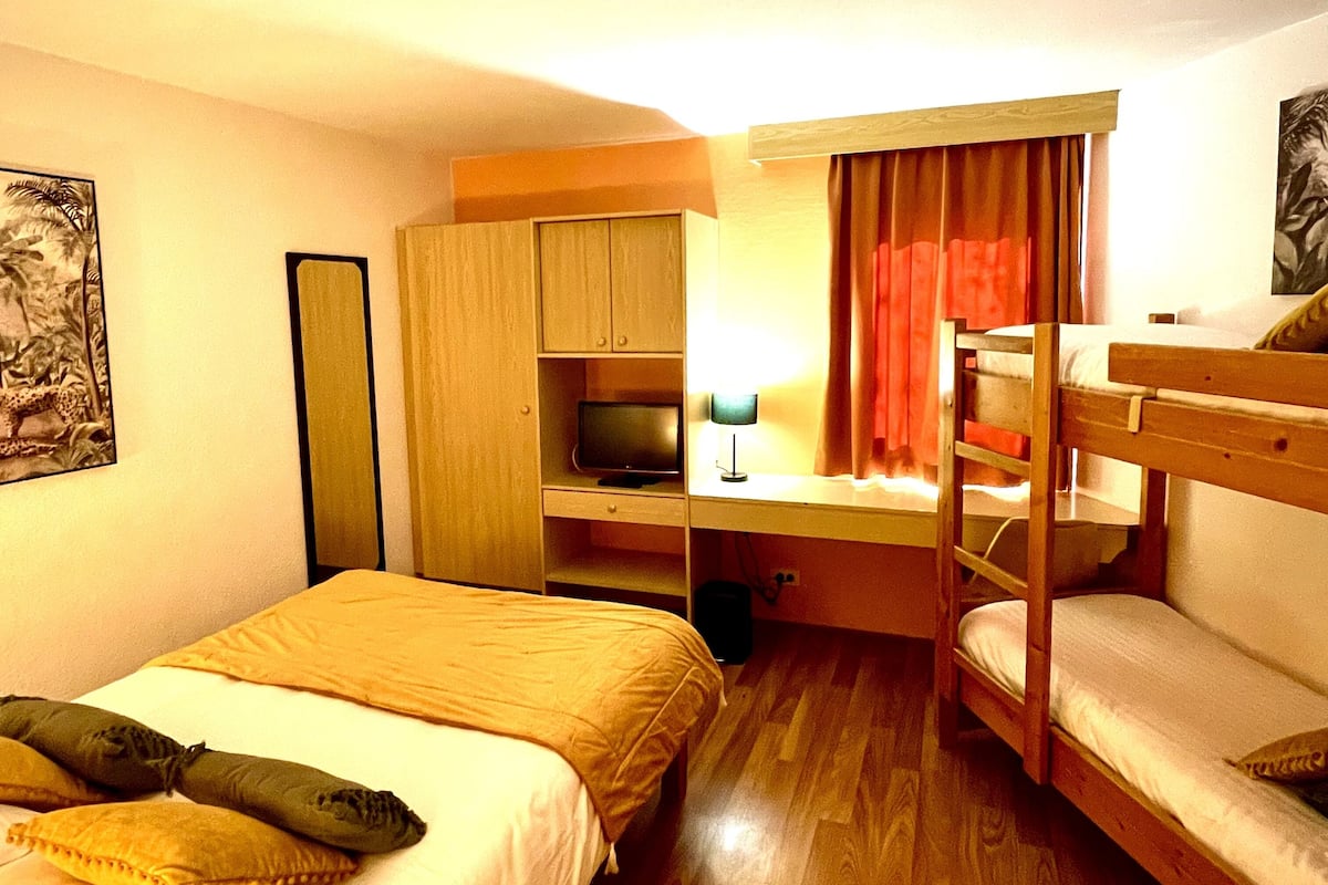 Une chambre avec un lit superposé, un bureau avec un ordinateur, une télévision et un lit avec des oreillers.