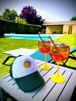 Mesa junto a la piscina con dos vasos de té helado y una gorra con un logotipo.