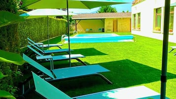 Patio con piscina, sillas de descanso y sombrillas.