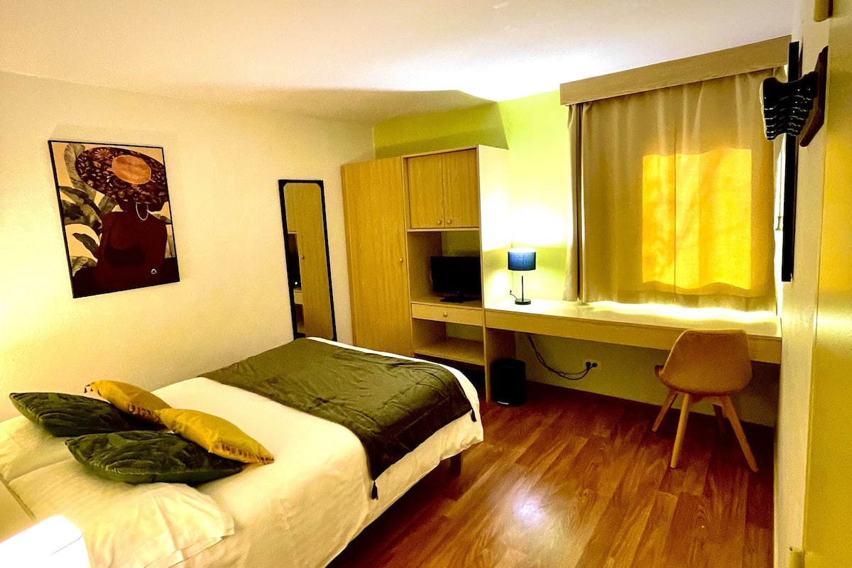 Une chambre à coucher avec un lit, un bureau, une chaise, une lampe et un tableau au mur.