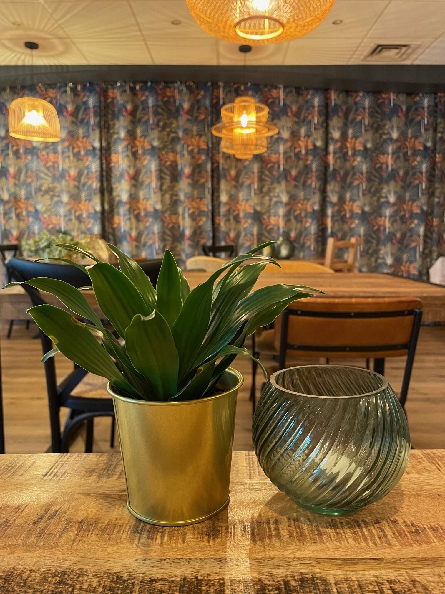 Una mesa con una planta en una maceta dorada y un jarrón de vidrio verde.