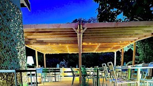 An outdoor patio area with tables and chairs, a wooden pergola, and a sign for the Mont Brouilly Hotel Restaurant. - Hôtel Restaurant Le Mont Brouilly (Quincie-en-Beaujolais)