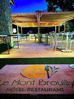 Un patio al aire libre con mesas y sillas, una pérgola de madera y un letrero del Restaurante Hotel Mont Brouilly.
