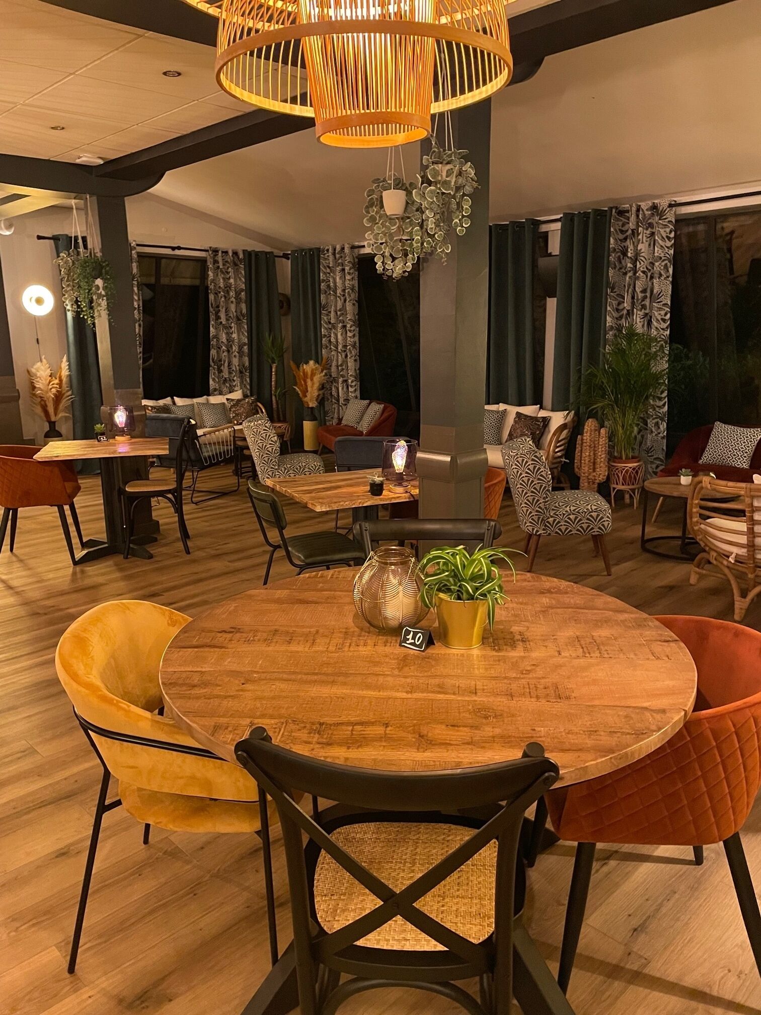 A modern dining area with a round wooden table, cushioned chairs, and a hanging light fixture.