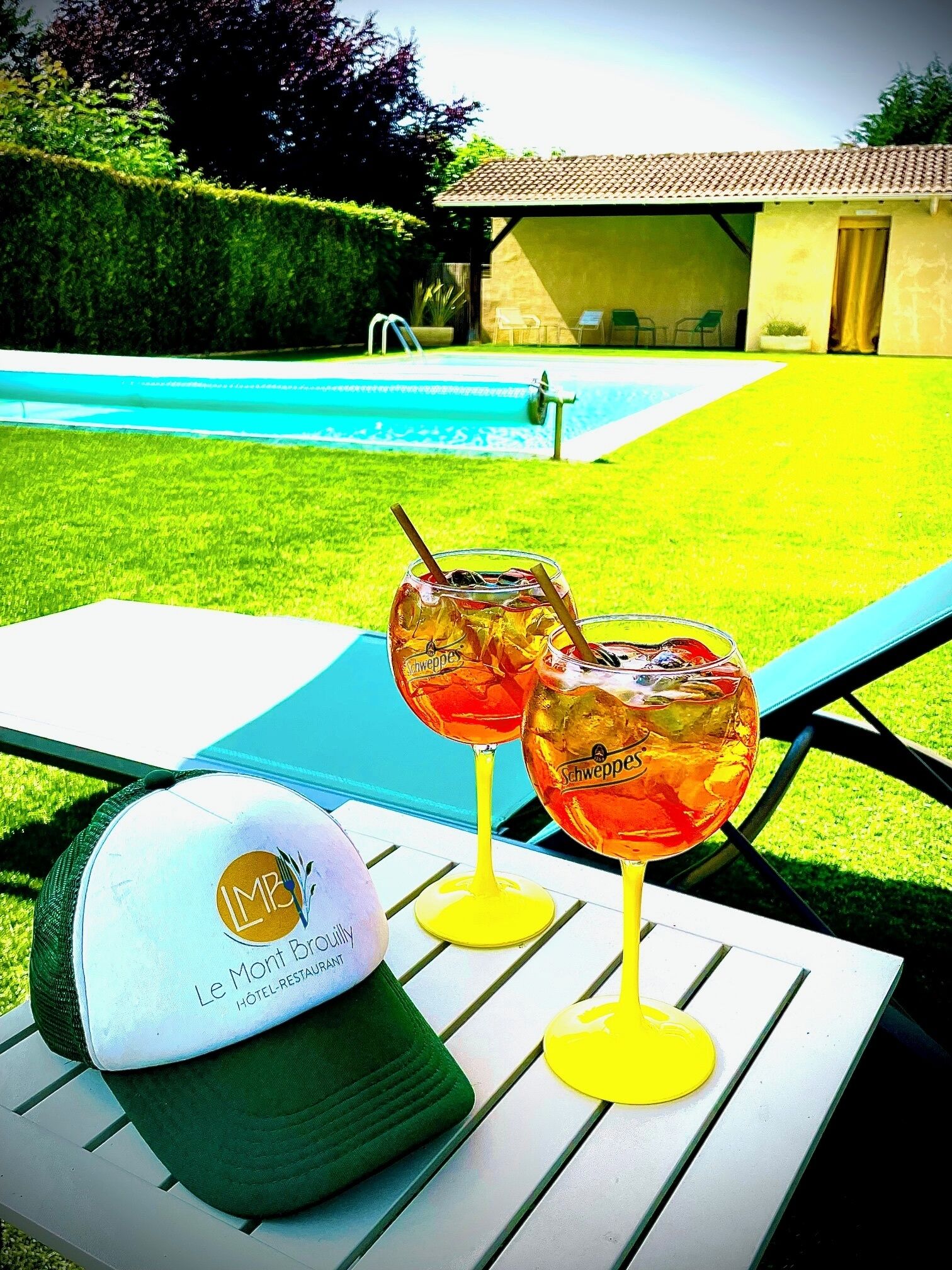A poolside setting with a table, two glasses of a beverage, and a cap.