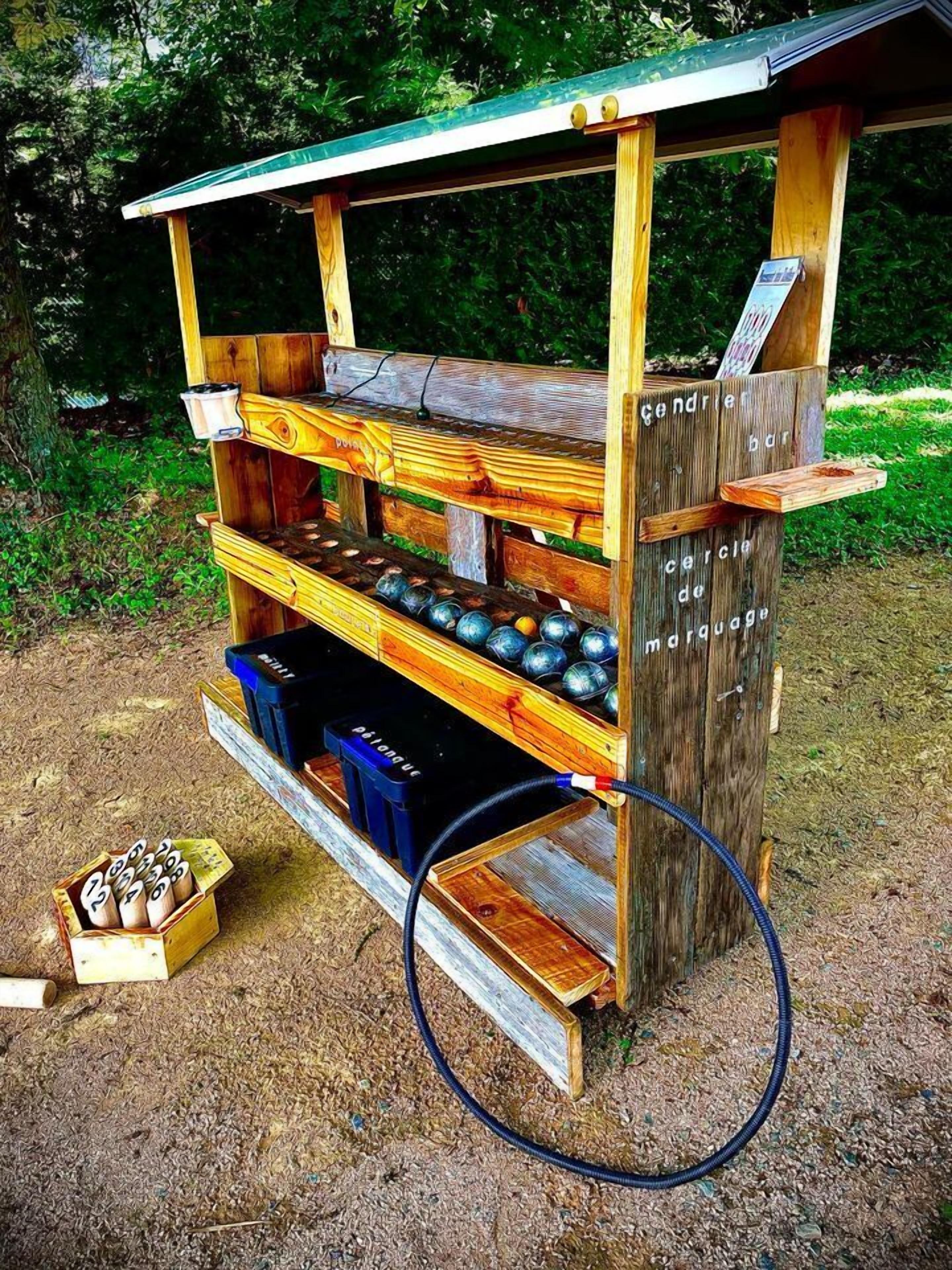 Un stand de jeux d’extérieur en bois, avec des boules numérotées et une pancarte indiquant : « cendrier bar cercla de maquette ».