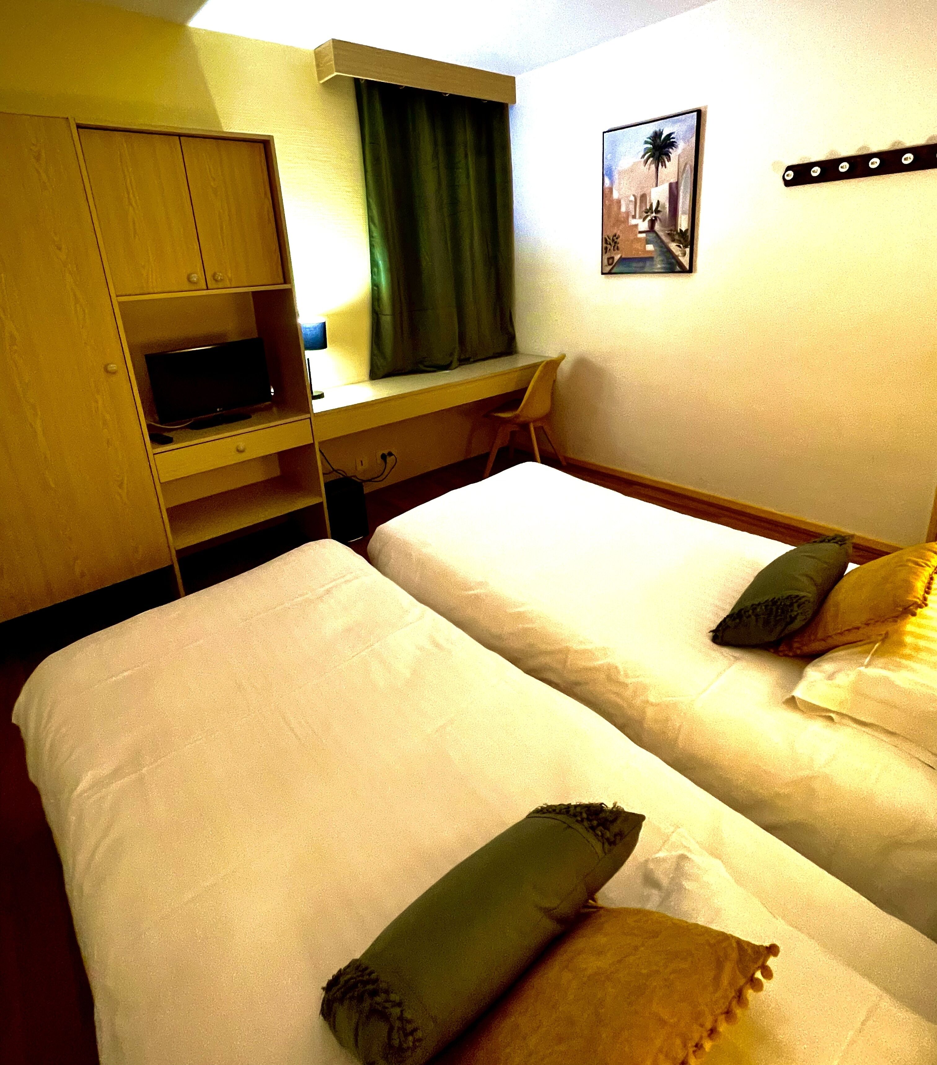 A hotel room with two beds, a desk, a chair, and a television.