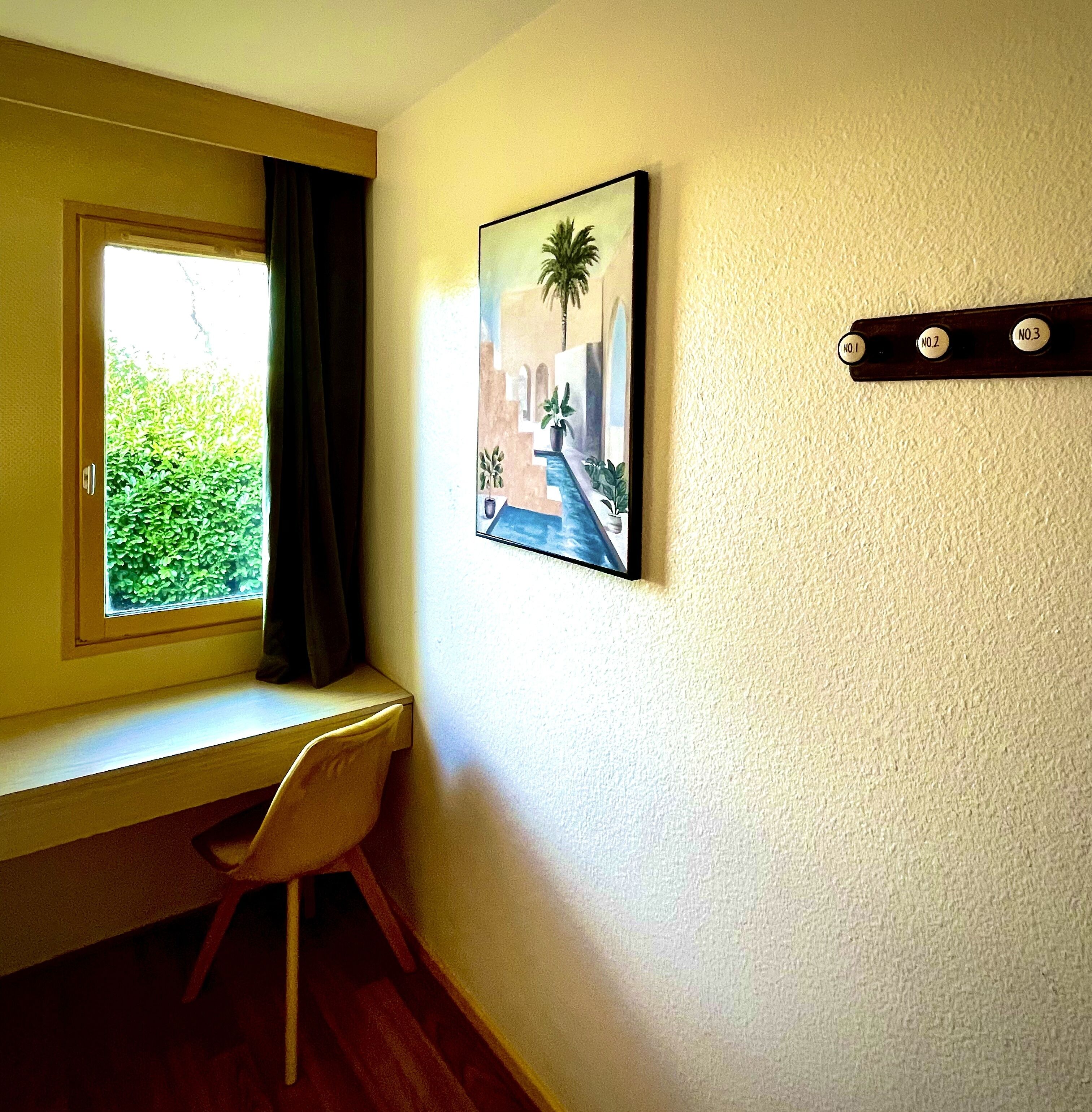 Een kamer met een bureau, een stoel, een raam met gordijnen en een aan de muur hangend schilderij.