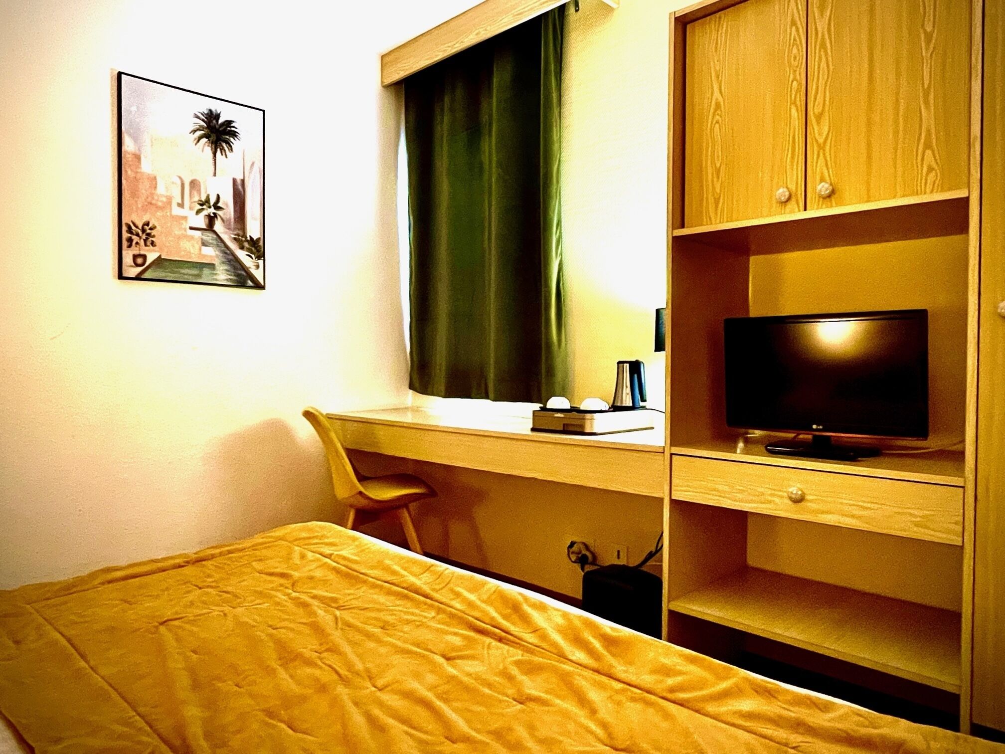 A hotel room with a bed, a desk with a computer and a TV, a chair, and a window with curtains.
