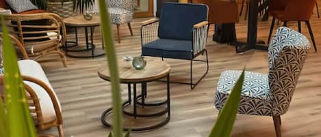 A modern lounge area with a variety of seating options including sofas, chairs, and a dining table. There are potted plants and a visible exit door.