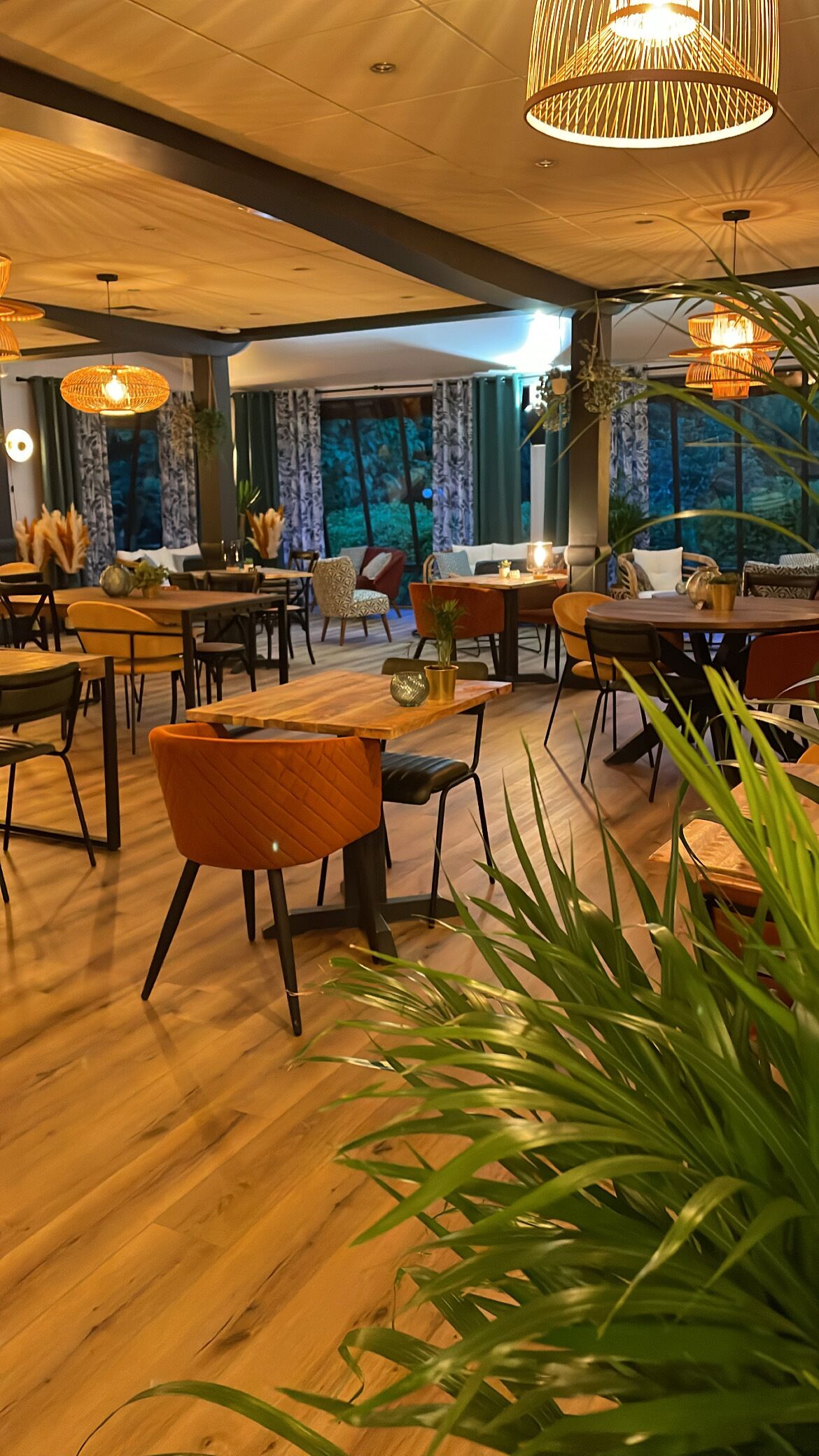 Un restaurante con suelo de madera, varias mesas y sillas, y lámparas colgantes de mimbre.