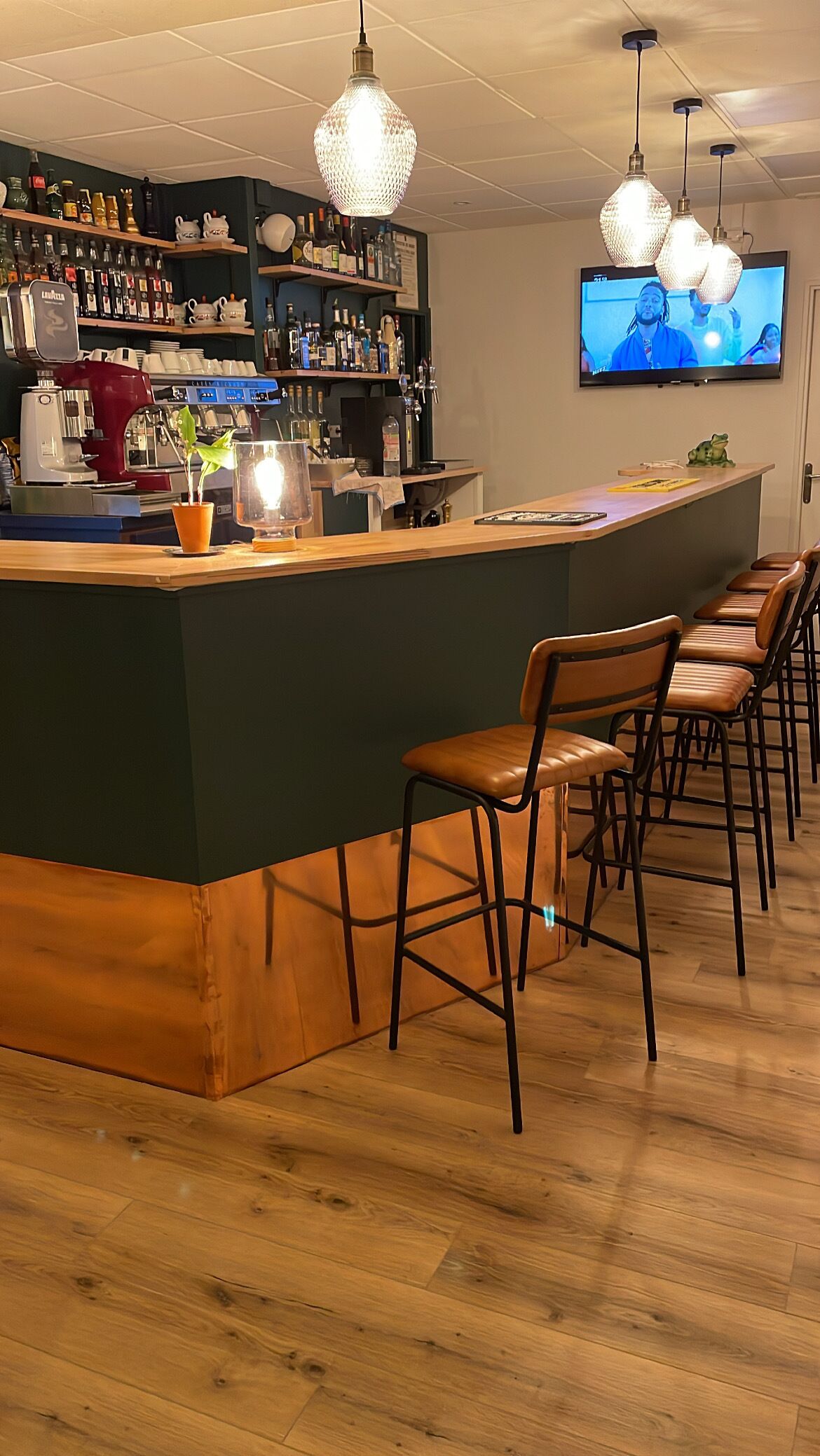 Zona de bar con mostrador, taburetes, televisor y varios botellas y vasos en estantes.