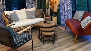 A modern living room with a sofa, armchair, and coffee table, featuring patterned curtains and a large window with a view of greenery. - Hôtel Restaurant Le Mont Brouilly (Quincie-en-Beaujolais)