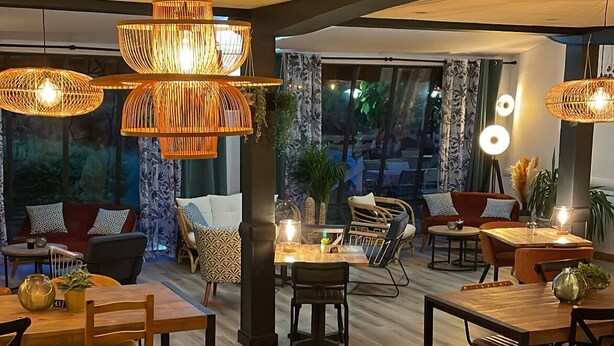 A modern dining area with wooden tables and chairs, hanging wicker chandeliers, and large windows offering a view of the outdoors. - Hôtel Restaurant Le Mont Brouilly (Quincie-en-Beaujolais)