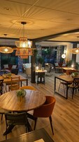 Un comedor moderno con mesas y sillas de madera, lámparas colgantes de mimbre y ventanas amplias que ofrecen vistas al exterior.